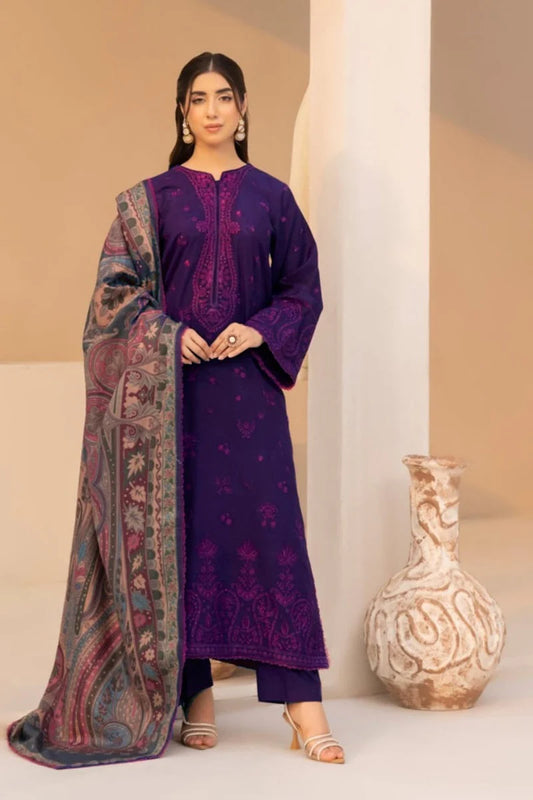 Woman wearing a purple embroidered outfit with a patterned shawl, standing next to a decorative vase.
