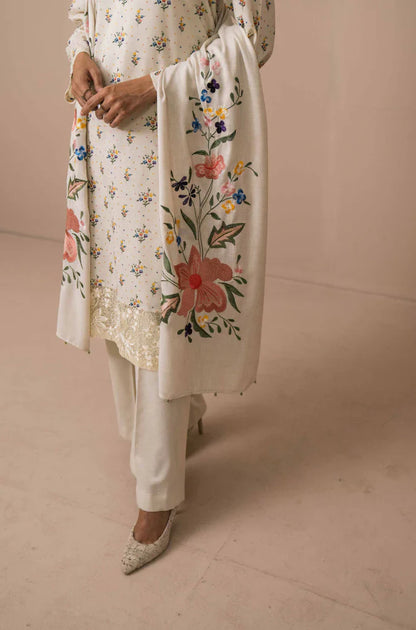 Person wearing a floral embroidered kurta with white pants on a beige background