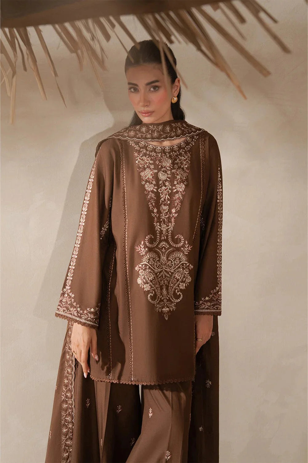 Woman wearing a brown embroidered outfit against a neutral background