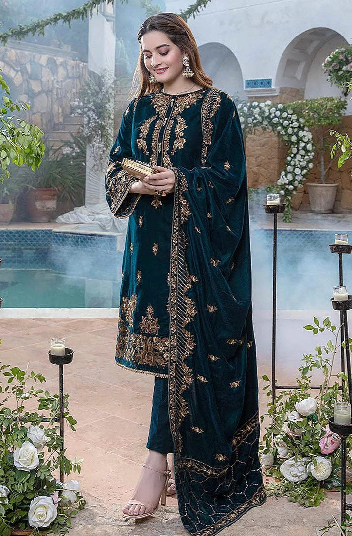 Woman in a teal embroidered outfit standing by a poolside with decorative plants and flowers.