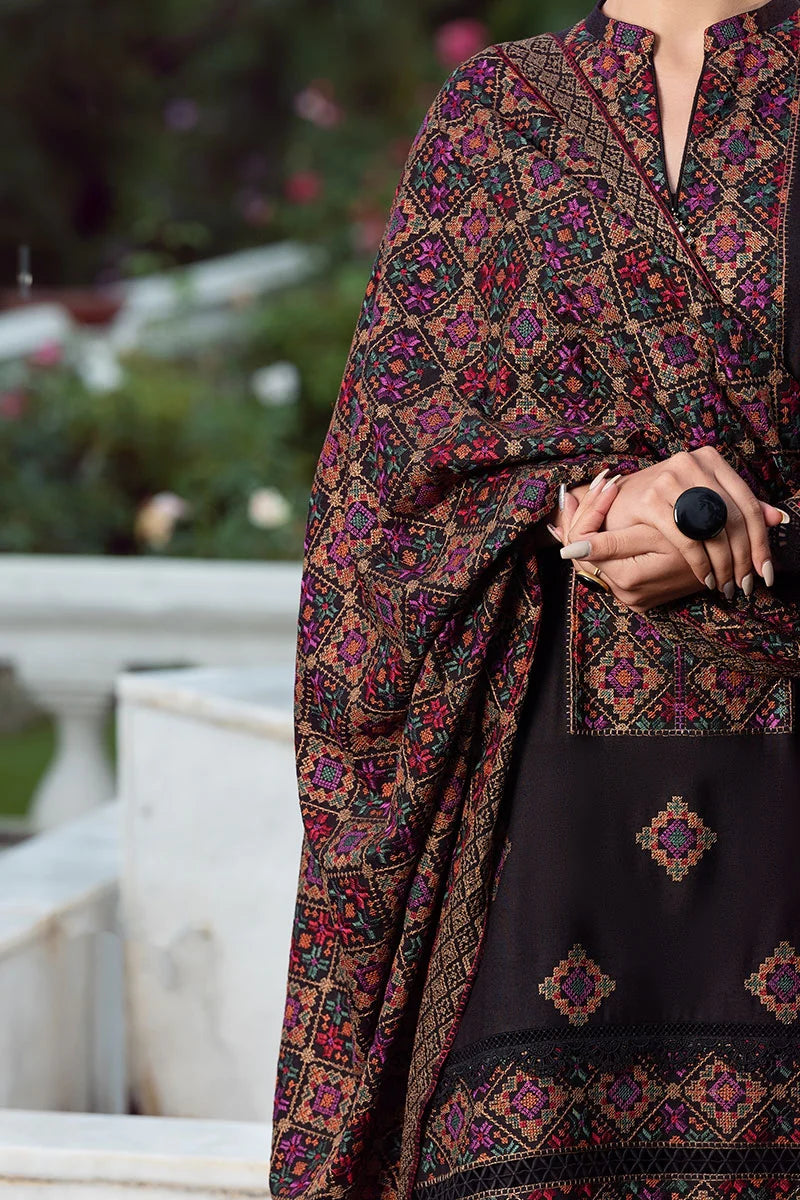 Person wearing a black and patterned traditional outfit with a blurred outdoor background