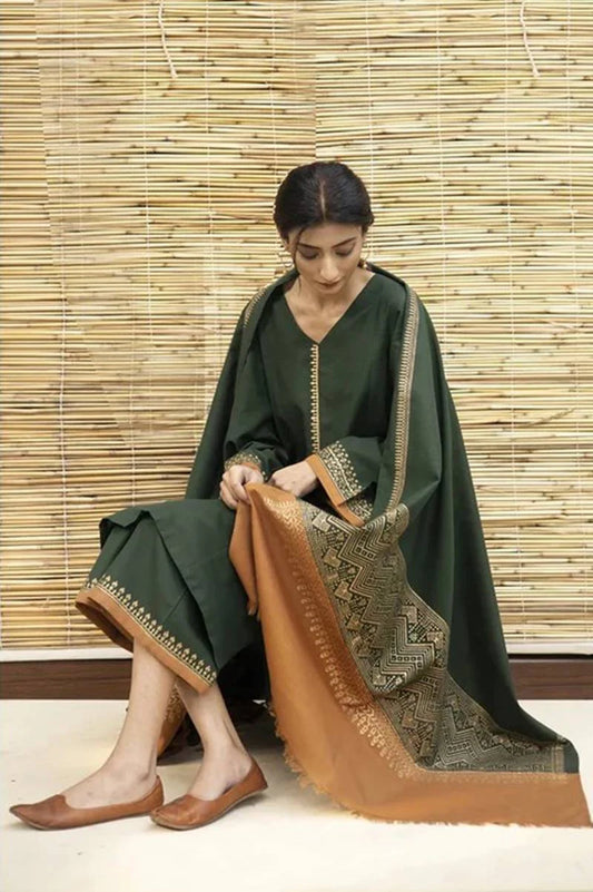 Woman in a green traditional outfit with a brown patterned scarf against a bamboo wall.